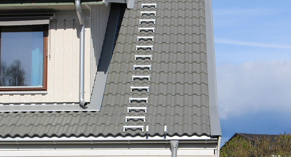 Detalj av ett tak med grå takpannor och takstege monterad längs takets lutning, med en takfot och stuprör i nederkant.