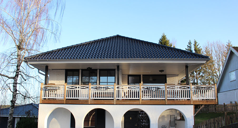 us med mörkt valmat tak och en stor balkong med räcke, ovanför en bottenvåning med valvbågar.