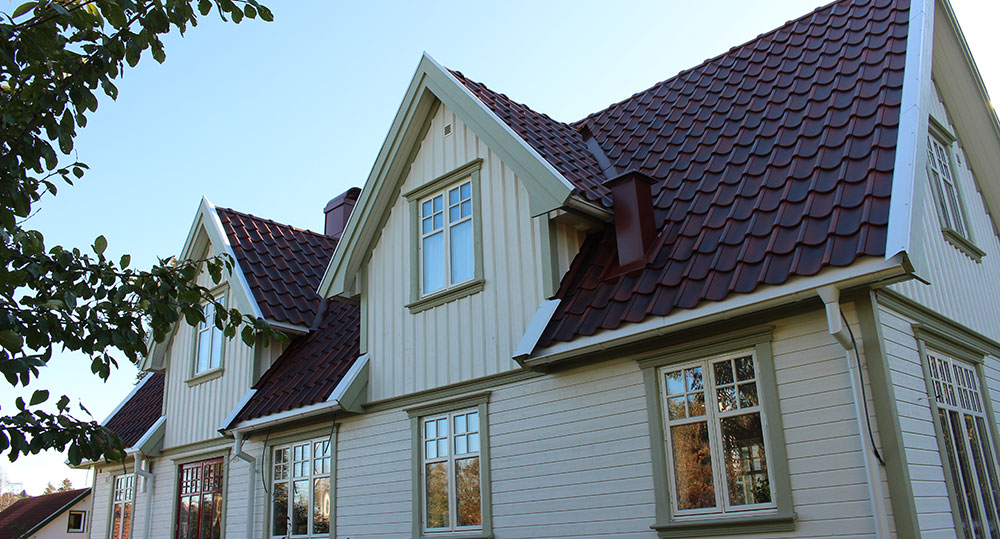 Vit villa med rött tegeltak, flera takkupor och stora fönster, fotograferad snett underifrån mot en klar himmel.